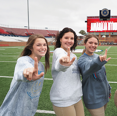 三名学生在足球场上举着代表美洲虎的J标志.