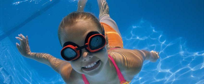 戴着护目镜微笑着在水下游泳的女孩.